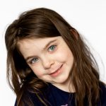 School Photo of brown haired girl against white background smiling and tilting her head to the left