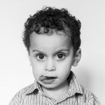 Black and white photo of toddler boy sticking his tongue out during school photo