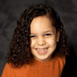 Photo of girl in orange shirt against dark gray background taken during school's picture day