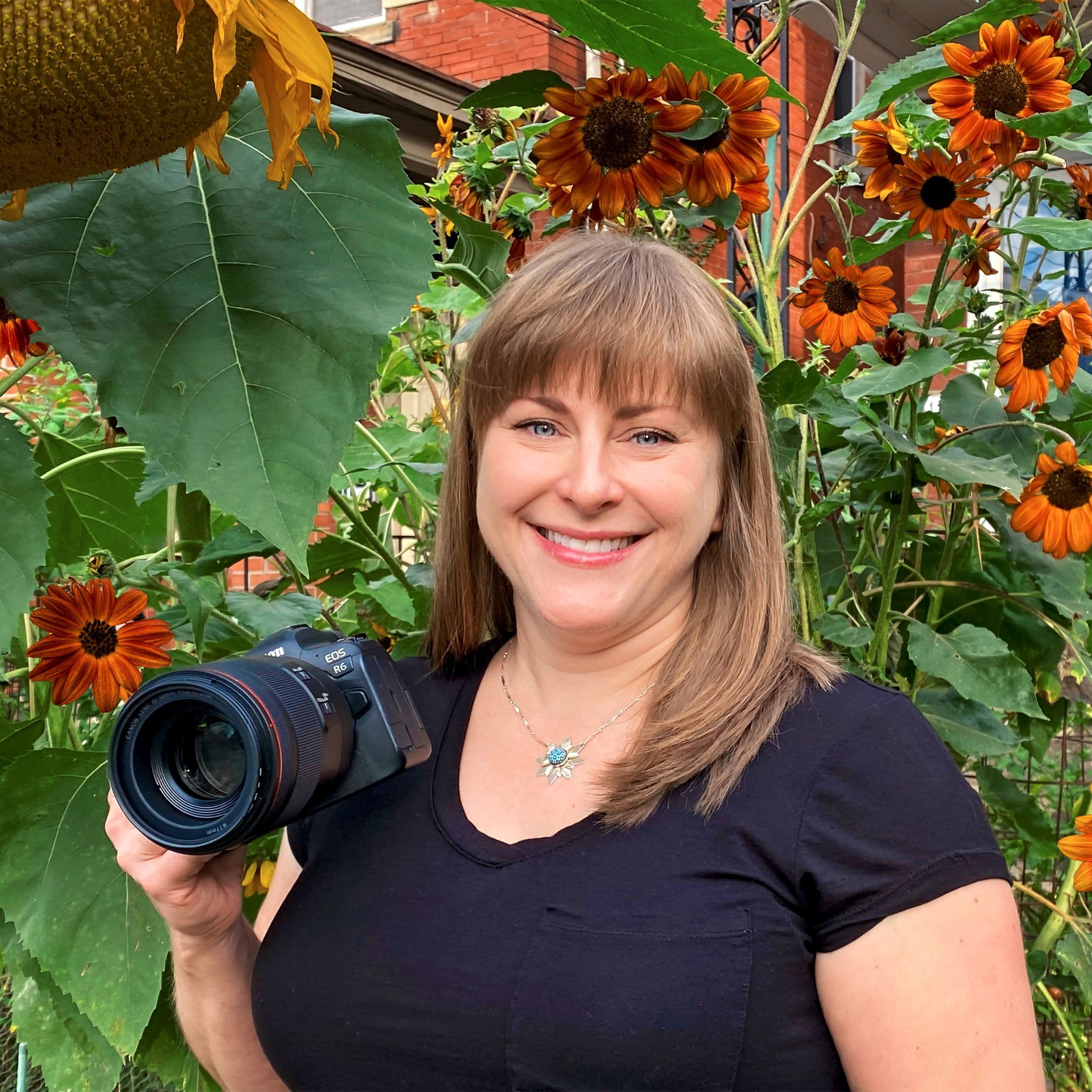 Carey Palenchar of Carey Palenchar Photography poses in her front yard garden full of sunflowers and holds her camera