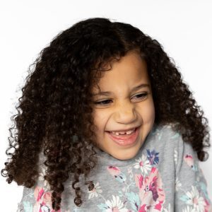 Modern School Picture of girl with curly hair and floral shirt smiling against a white background