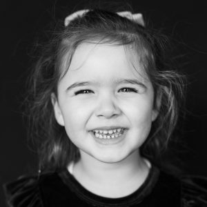 Black and white modern school portrait of smiling girl with black background